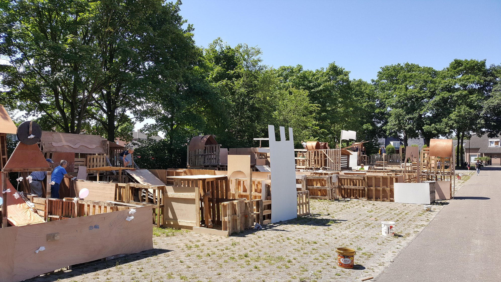 Overzicht van veel houten bouwwerken met 2 begeleiders er bij en 1 kind die van de glijbaan af gaat.